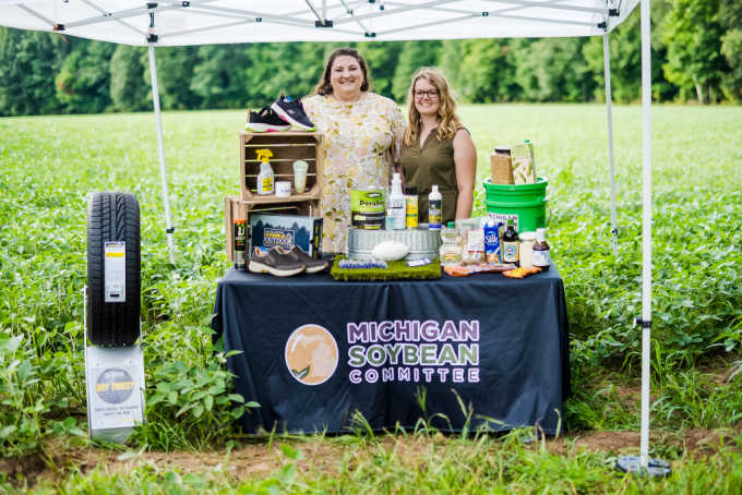 Michigan Soybean Committee standing behind their table of soy products next to a soy field