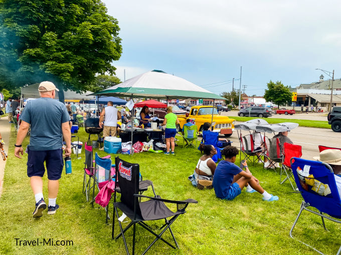 People sitting in chairs, on the ground and under tents along Woodward Avenue