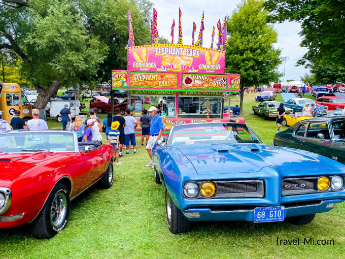 Red and blue classic cars in front of a vendor selling elephant ears and funnel cakes